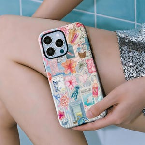 May include: A phone case with a coastal-themed design. The case features a collage of images including seashells, flowers, and a pink gummy bear. The words "Coastal Life" are visible on a magazine cover. The background has white and blue stripes.