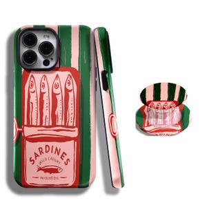 Puede incluir: Funda de teléfono con diseño de lata de sardinas. La funda presenta un fondo a rayas verdes y rosas con una ilustración de lata de sardinas roja. La lata dice "Sardines Wild Caught in Olive Oil" con un gráfico de pez.