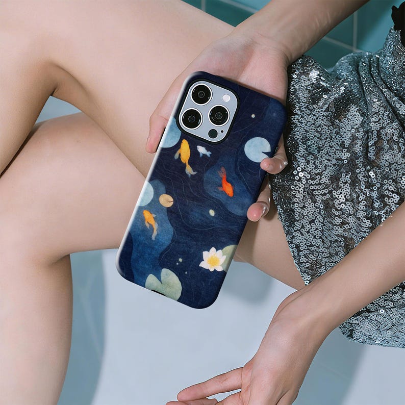 May include: A navy blue phone case featuring a koi pond design. The case has a dark blue background with yellow, orange, and white koi fish, lily pads, and a white lotus flower. The case has a glossy finish.