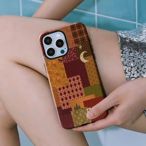 May include: A patchwork-style phone case in shades of brown, orange, and red. The case features a variety of patterns, including plaid, stars, and floral designs. A crescent moon and stars are also visible on the case.