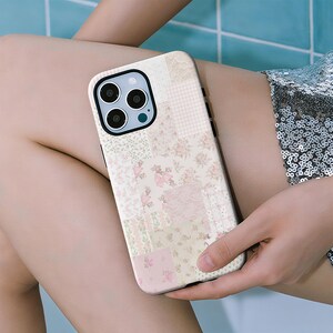 May include: A patchwork phone case featuring a mix of floral and gingham patterns in soft pink, cream, and beige tones. The case has a black border and a camera cutout.