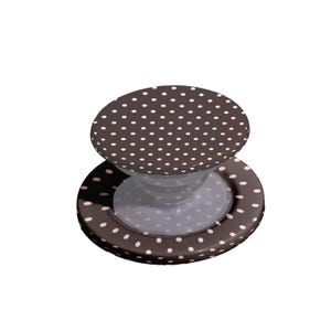 Pode incluir: Um suporte de telefone castanho e branco com bolinhas. A pega tem uma base circular e um topo redondo, ambos decorados com bolinhas brancas. A pega foi concebida para ser fixada na parte de tr&aacute;s de um telefone.