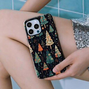 Puede incluir: Funda negra para smartphone con un patrón repetido de árboles de Navidad coloridos. Los árboles son verdes, naranjas y blancos, con pequeños detalles florales y de hojas. La funda tiene un acabado brillante.