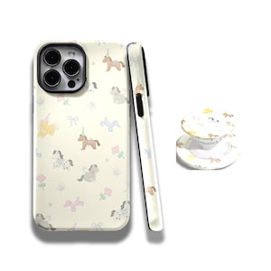 May include: A phone case and pop socket set with a cream background and a repeating pattern of pastel-colored horses, bows, and flowers. The phone case is shown with a black camera lens and a black border. The pop socket is round and has a matching design.