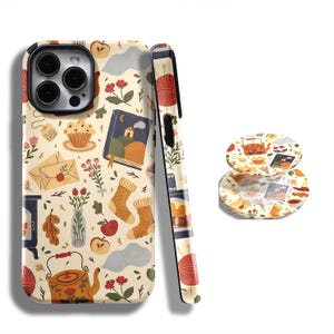 Op de afbeelding: Een telefoonhoesje en twee onderzetters met een crèmekleurige achtergrond en een herhalend patroon van gezellige herfstillustraties. Het ontwerp bevat een theepot, sokken, een boek en andere herfstthema-elementen.