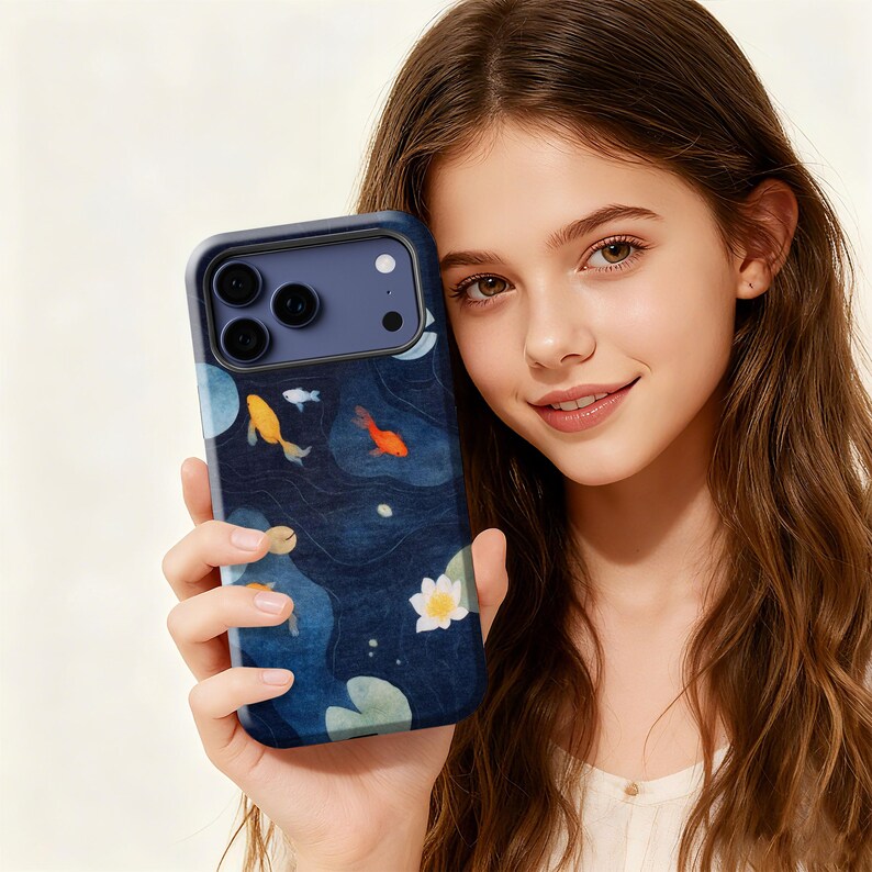 May include: A navy blue phone case featuring a koi pond design. The case displays yellow and orange koi fish swimming among lily pads and white flowers. The case has a dark blue border and a camera cutout.