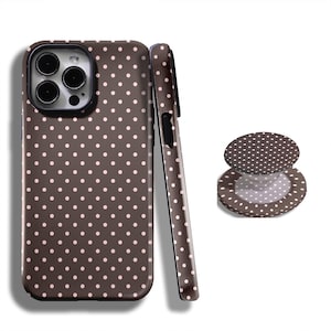 May include: A brown phone case and matching phone grip with a white polka dot pattern. The phone case is shown upright and on its side, with the grip extended and collapsed. The phone case has a camera cutout.