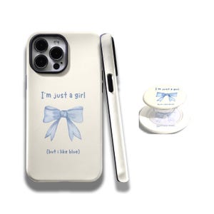 Pode incluir: Capa de telefone e pop socket branco sujo com um laço azul e o texto "I'm just a girl (but I like blue)". A capa tem uma lente de câmera preta e uma borda preta.