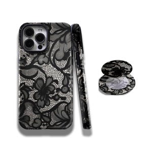 Puede incluir: Funda de teléfono y pop socket a juego con estampado de encaje negro y blanco. La funda del teléfono se muestra desde varios ángulos, destacando el intrincado diseño floral. El pop socket es redondo y presenta el mismo patrón de encaje.