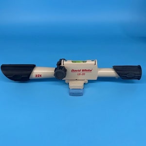 May include: A beige David White L6-20 level with black rubber grips and a bubble level. The level has the text "22X" and "David White L6-20" printed on it. The background is a solid blue.