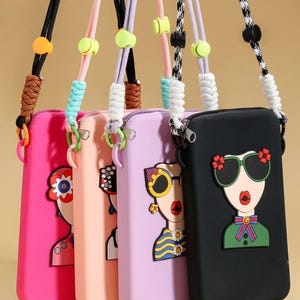 May include: Four rectangular crossbody phone pouches in hot pink, peach, lavender, and black. Each features a raised silicone graphic of a face wearing sunglasses and colorful clothing. The bags have adjustable rope straps with plastic toggles.