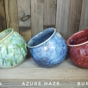 Può includere: Tre ciotole in ceramica di diversi colori: verde, blu e bordeaux. Le ciotole sono tutte inclinate di lato e hanno un bordo bianco.