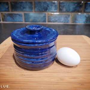 Op de afbeelding: Een blauwe keramische container met een deksel en een wit ei op een houten oppervlak.  BLUE.