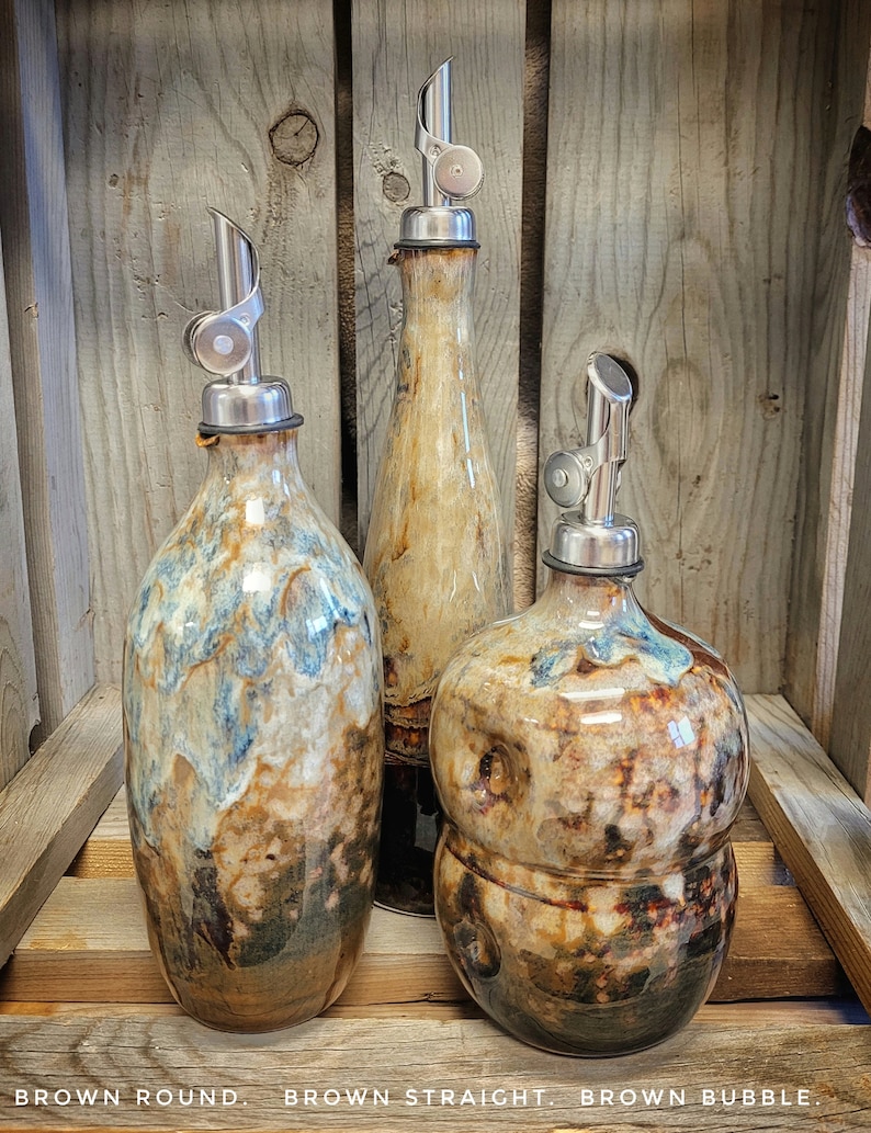 May include: Three ceramic oil and vinegar bottles with metal pour spouts. The bottles are brown, tan, and white with a mottled glaze. The bottles are labeled "Brown Round", "Brown Straight", and "Brown Bubble".