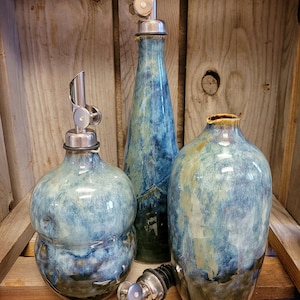 Puede incluir: Tres botellas de cer&aacute;mica para aceite y vinagre con boquillas de vertido plateadas. Las botellas son de esmalte azul y verde con un efecto moteado. Las botellas est&aacute;n etiquetadas como "Peacock Bubble", "Peacock Straight" y "Peacock Round".