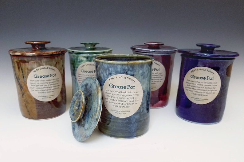 Pode incluir: Cinco potes de gordura de cer&acirc;mica com tampas. Os potes s&atilde;o decorados com diferentes esmaltes e t&ecirc;m etiquetas que dizem "Abby Lingle Pottery" e "Grease Pot".