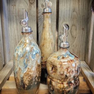 Puede incluir: Tres botellas de cer&aacute;mica para aceite y vinagre con boquillas de vertido de metal. Las botellas son marrones, beige y blancas con un esmalte moteado. Las botellas est&aacute;n etiquetadas como "Brown Round", "Brown Straight" y "Brown Bubble".