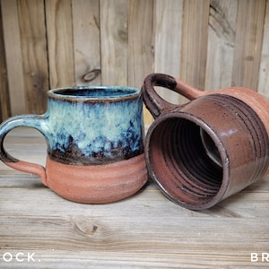 Könnte beinhalten: Zwei Keramikbecher, einer mit blauer und brauner Glasur und der andere mit brauner Glasur. Die Becher stehen auf einer Holzoberfläche. Der Text "PEACOCK" ist auf der linken Seite des Bildes und der Text "BROWN" auf der rechten Seite des Bildes sichtbar.