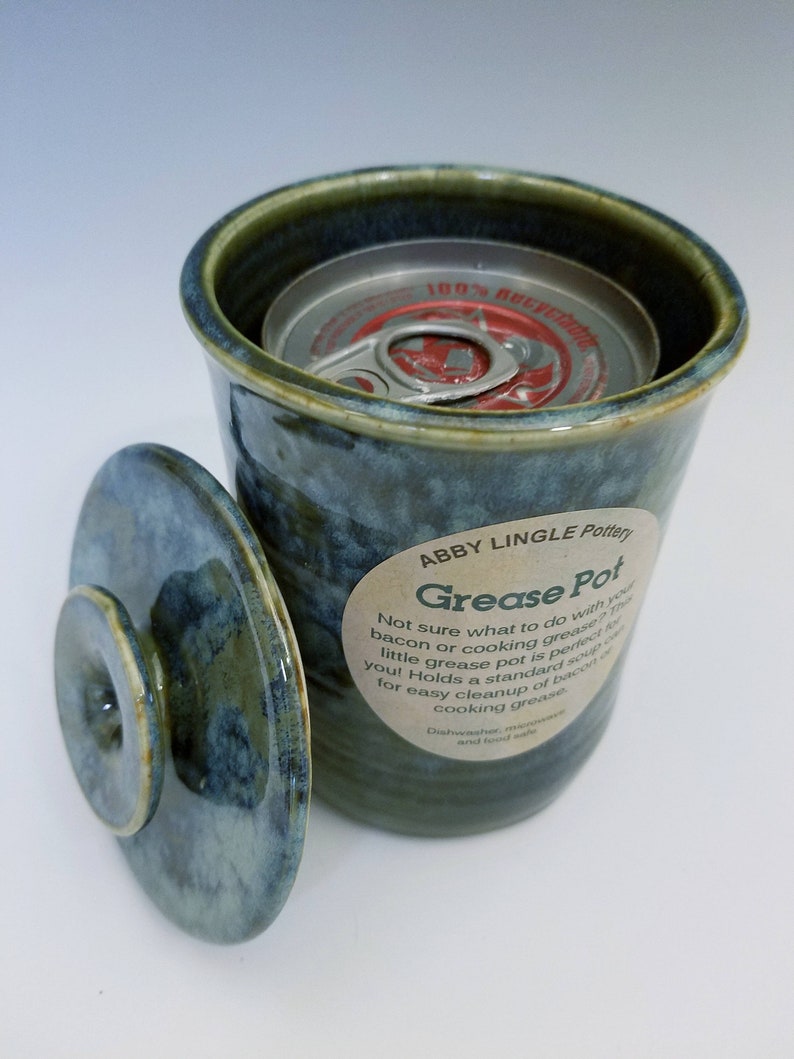 Pode incluir: Um pote de gordura de cer&acirc;mica verde e azul com tampa. O pote &eacute; feito para conter uma lata de sopa padr&atilde;o para uma f&aacute;cil limpeza de bacon ou gordura de cozinha. O r&oacute;tulo diz "Abby Lingle Pottery Grease Pot".