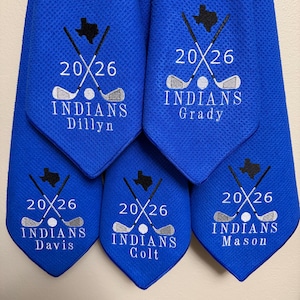 K&ouml;nnte beinhalten: Blaue Golfhandt&uuml;cher mit gestickten Designs. Jedes Handtuch zeigt den Text "20/26", gekreuzte Golfschl&auml;ger, einen Golfball und das Wort "INDIANS" zusammen mit einem Namen. Eine Texas-Umrisslinie ist ebenfalls gestickt.