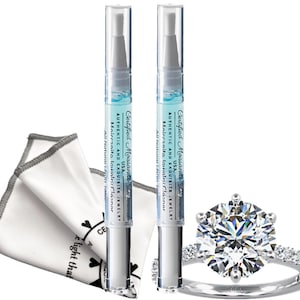 May include: A diamond ring with a large, clear center stone and smaller stones on the band, next to two jewelry cleaner pens and a white cleaning cloth. The pens have text that reads "Certified Moissanite Diamond".