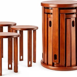 May include: A set of five round wooden stools with a smooth, reddish-brown finish. Each stool features four straight legs with a small oval cutout near the base. The stools are designed to stack vertically into a single cylindrical tower unit.