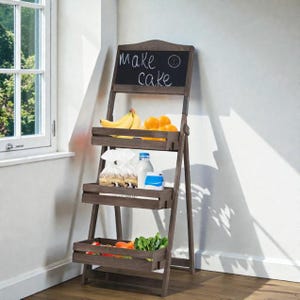 Könnte beinhalten: Ein dreistufiges Aufbewahrungsregal aus dunkelbraunem Holz mit einer Tafel oben. Auf der Tafel steht "Make a cake". Die Regale enthalten Bananen, Orangen, Lebensmittel und Gemüse. Das Regal steht an einer weißen Wand.