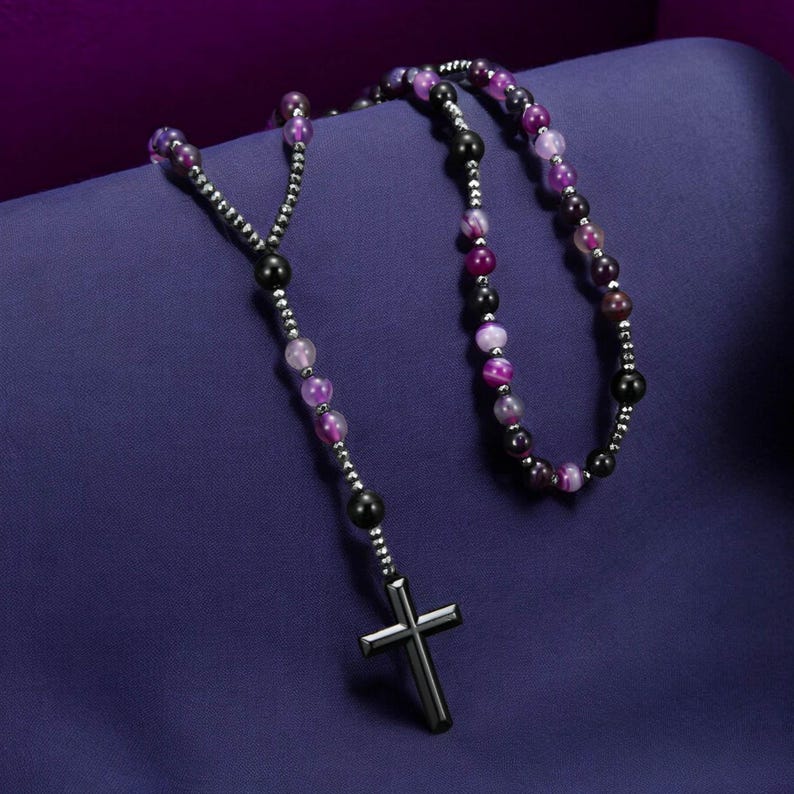 May include: A rosary necklace featuring a silver cross pendant and beads in shades of purple, black, and silver. The beads are strung on a silver chain, creating a religious accessory.