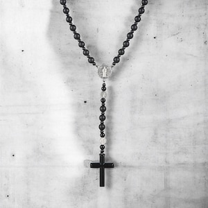 Puede incluir: Collar de rosario negro con cuentas mate y un centro y colgante de cruz plateados. El collar presenta una serie de cuentas redondas conectadas por una cadena, con una cruz en la parte inferior. El centro tiene un dise&ntilde;o detallado.