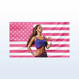 Pode incluir: Uma bandeira americana rosa e branca com uma mulher em um top azul e calças escuras. A bandeira tem listras brancas e estrelas rosa. A mulher está em frente à bandeira.