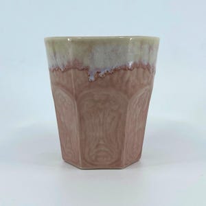 May include: A ceramic cup with a unique design. The cup has a light brown exterior with a textured pattern and a light beige rim. The cup's shape is a faceted, geometric design. The cup is suitable for hot or cold beverages.
