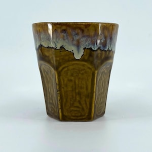 May include: A brown ceramic cup with a unique, geometric design. The cup has a textured surface and a glossy finish. The top edge features a glaze that transitions from brown to white and blue. The cup is suitable for hot or cold beverages.