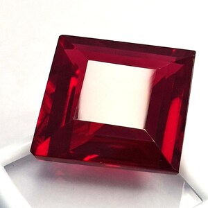 May include: A faceted, square-cut, deep red gemstone with a white square center. The gemstone is set against a white background, showcasing its clarity and brilliance. The edges of the gemstone are sharply defined.