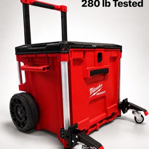 Könnte beinhalten: Ein roter und schwarzer Milwaukee Packout Rollwerkzeugkasten mit Teleskopgriff, großen schwarzen Rädern und zwei vorderen Lenkrollen. An der Seite befindet sich der Text Static load 280 lb Tested sowie das weiße Milwaukee Packout Logo.