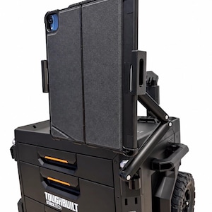 May include: A black ToughBuilt StackTech mobile tool chest with orange accents and a tablet mount attached to the side. The tablet is held in a dark gray folding case, positioned vertically on an adjustable arm extending from the tool storage unit.