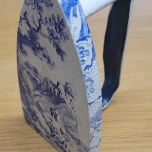 Peut inclure: Objet décoratif en forme de fer à repasser, avec une poignée blanche et un motif de toile de Jouy bleu et blanc sur la base. La poignée est blanche, et l'intérieur est bleu foncé.