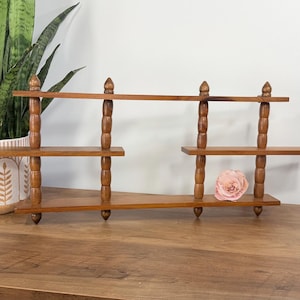 May include: A vintage wooden shelf with three tiers and decorative finials. The shelf is a warm brown color and has a unique, tiered design. A potted snake plant and a pink rose are also visible.