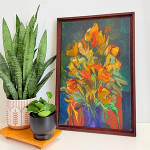 May include: A framed oil painting shows a vibrant bouquet of yellow, orange, and red flowers on a dark blue and green backdrop. A snake plant in a patterned pot and a small plant in a black pot sit on a wooden tray.