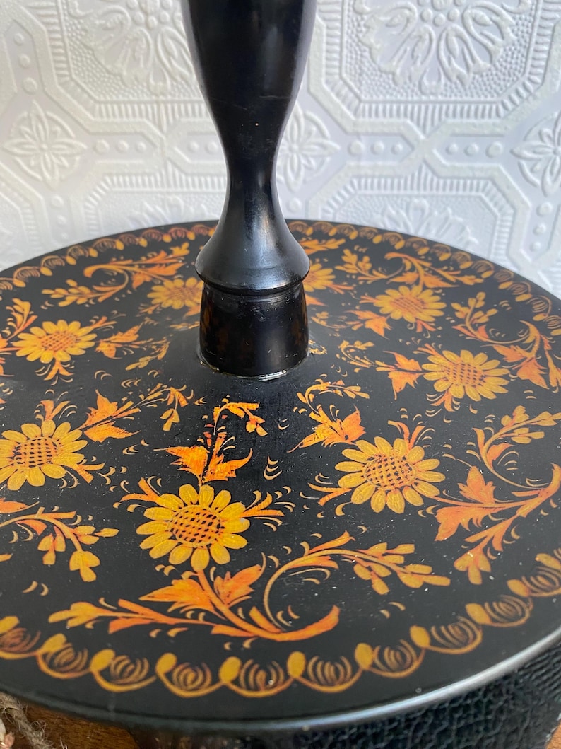 Pu&ograve; includere: Un vassoio decorativo rotondo nero con uno stelo centrale nero. Il vassoio &egrave; adornato con un motivo floreale giallo e arancione. I fiori e le foglie sono dipinti su uno sfondo nero.