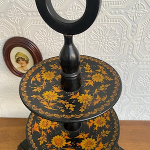 Pu&ograve; includere: Un vassoio nero a tre livelli con manico. Ogni livello &egrave; decorato con un motivo floreale giallo. Il vassoio &egrave; in legno ed &egrave; probabilmente vintage o antico.