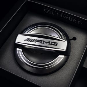 May include: A silver and black AMG fuel door cover, presented in a black box. The cover features the AMG logo and the word "OPEN" in white. The text "GEL HYBRID" is visible on the box.