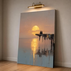 May include: A vertical rectangular canvas print featuring a sunset landscape with two silhouettes sitting on a cliff edge overlooking a calm body of water. The scene displays warm golden hues, a bright sun, and vertical paint drip textures.