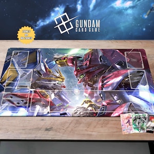 Może przedstawiać: Prostokątna mata do gry Gundam Card Game z ilustracją dwóch robotów mecha. Mata ma wyznaczone strefy na karty i tekst "ZONES OR NO ZONES". Widoczne jest logo Gundam Card Game.