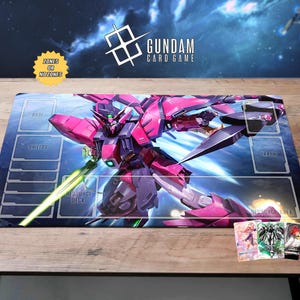 May include: A Gundam card game playmat featuring a pink and purple mech with a green energy sword. The mat has zones labeled for gameplay and the Gundam Card Game logo. Three cards are visible in the lower right corner.
