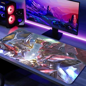 May include: A large rectangular gaming mouse pad featuring a detailed illustration of two robots in a battle scene. The robots are primarily red, gold, and silver, set against a backdrop of a futuristic landscape. The pad is on a desk with a computer monitor and PC tower.