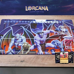 Puede incluir: Tapete de juego para el juego de cartas coleccionables Lorcana, con un fondo morado oscuro e ilustraciones de gárgolas. El tapete tiene áreas de juego y el logotipo del juego en la parte superior. Se muestran dos cartas.