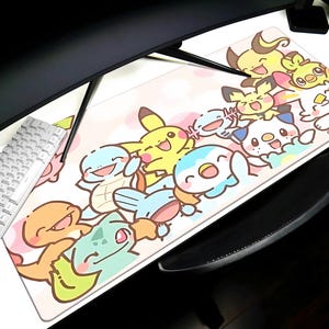 A colorful mouse pad featuring various cartoon Pokemon characters, including Pikachu, Charizard, Bulmer, and others, is placed on a desk alongside a keyboard and a mouse.