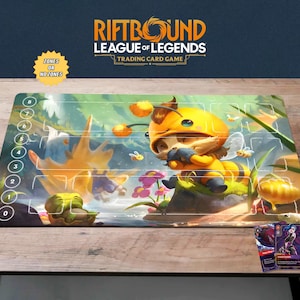Op de afbeelding: Een League of Legends trading card game speelmat met een cartoon bijenpersonage. De mat heeft een kleurrijk fantasielandschap ontwerp met zones gemarkeerd 0-8. De tekst "RIFTBOUND LEAGUE OF LEGENDS TRADING CARD GAME" staat bovenaan.