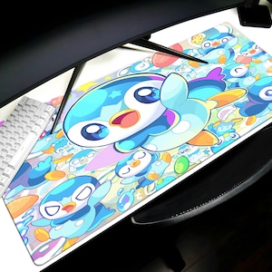 May include: A rectangular mouse mat with a cartoon design of a blue penguin with large eyes and a yellow beak. The mat has a white background with other cartoon penguins and water droplets. A white keyboard is visible.