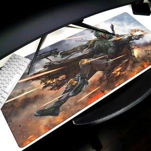 May include: A rectangular desk mat featuring a dynamic illustration of a character in a green and gray suit, firing a weapon amidst an action scene with orange and yellow explosions. A white keyboard and black wrist rest are also visible.